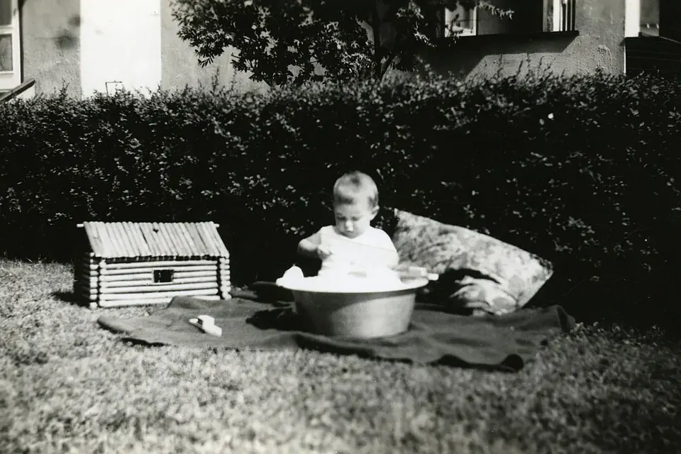 Photographie ancienne en noir et blanc d'un jeune enfant jouant dans l'herbe derrière une maison