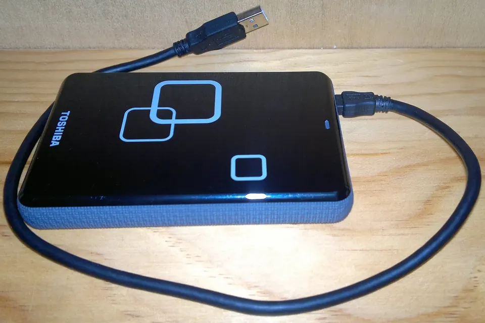Disque dur externe portable noir posé sur une surface claire, câble USB branché