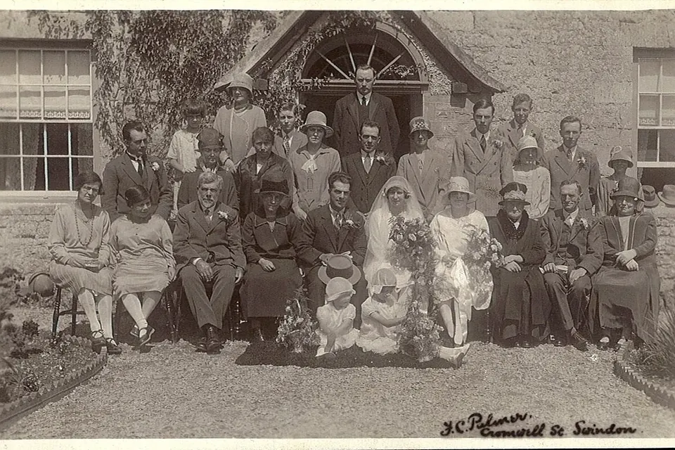 Photographie ancienne d'un mariage anglais : les mariés entourés de leur famille posent en deux rangs devant une maison